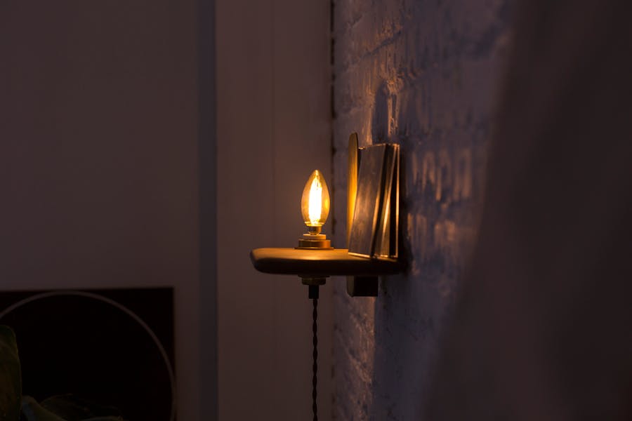 Matte black wall sconce with an exposed bulb casting warm light on a textured indoor wall